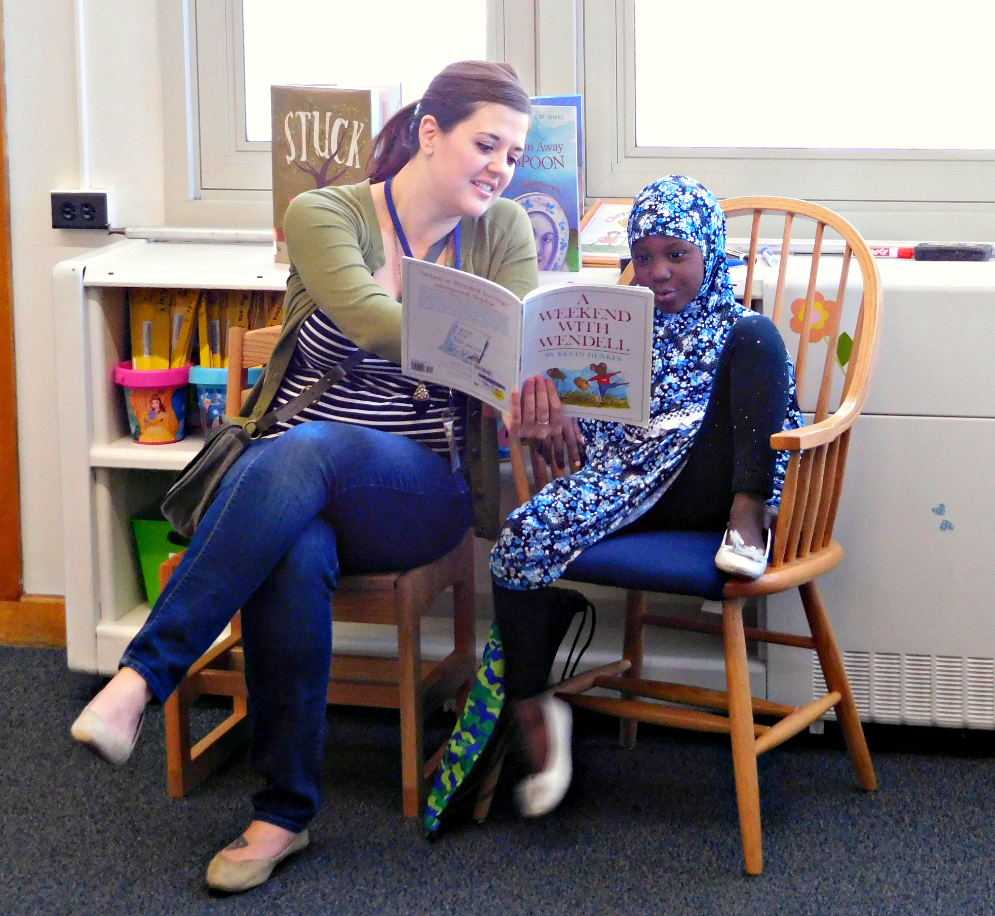 DPS Volunteer reading with student near windows 